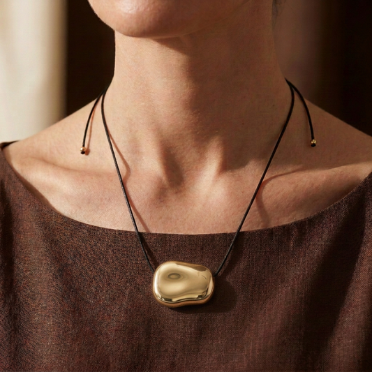 Collar Sienna dorado puesto, con cordón largo y estilismo en tonos marrón chocolate.