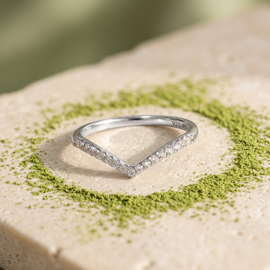 Anillo plateado en V con un toque de polvo matcha sobre fondo crema