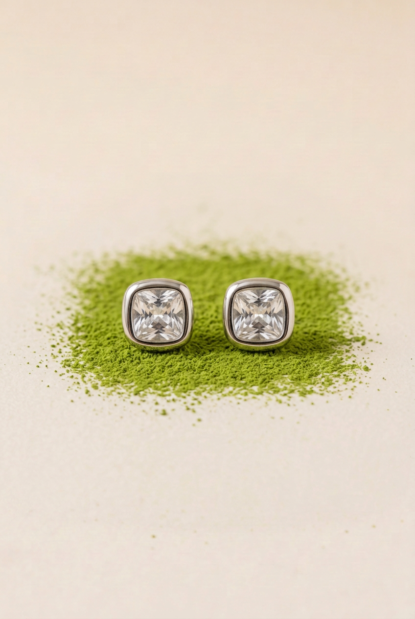 Aretes plateados con piedras claras sobre matcha en polvo y fondo marfil