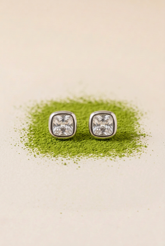 Aretes plateados con piedras claras sobre matcha en polvo y fondo marfil