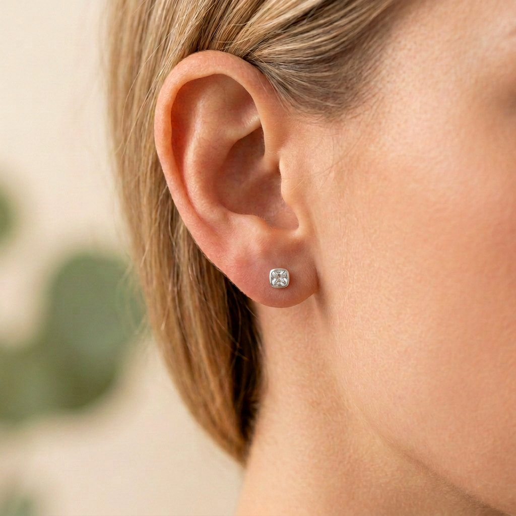 Arete plateado pequeño con piedra clara puesto en la oreja, con luz suave y estilo minimalista