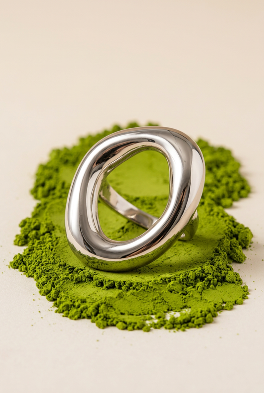 Anillo ovalado plateado sobre polvo de matcha, estilo editorial.